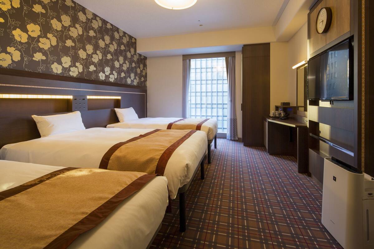 Habitación de hotel con tres camas, un televisor, un reloj y una ventana con cortinas.