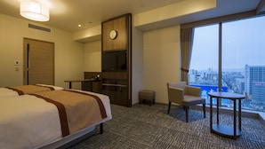 A hotel room with two beds, a desk, a chair, a clock, and a large window with a city view.