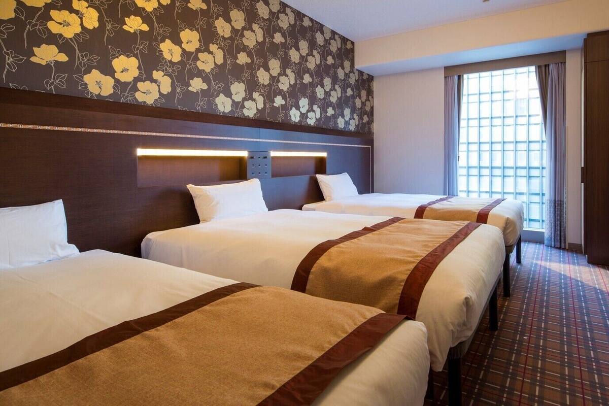 Habitación de hotel con tres camas, un ventanal grande y un papel tapiz estampado.