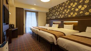 A hotel room with three beds, a desk with a computer, a clock, and a window with curtains.