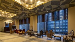 A spacious lobby with a checkered floor, large windows with a city view, and a variety of seating options including armchairs and sofas.