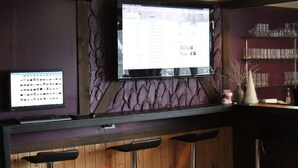 A bar area with a computer monitor displaying a webpage, a television screen, and a shelf with glasses. - Alpine Lodge (Hakuba)
