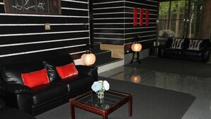 A modern living room with a black leather sofa, red cushions, a glass coffee table with a vase of flowers, and a black and white striped wall with red accents. - Alpine Lodge (Hakuba)