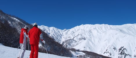 A snowy mountain landscape with skiers in red jackets.