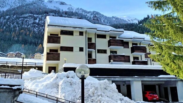 A multi-story building with a snow-covered roof, surrounded by mountains and trees.
