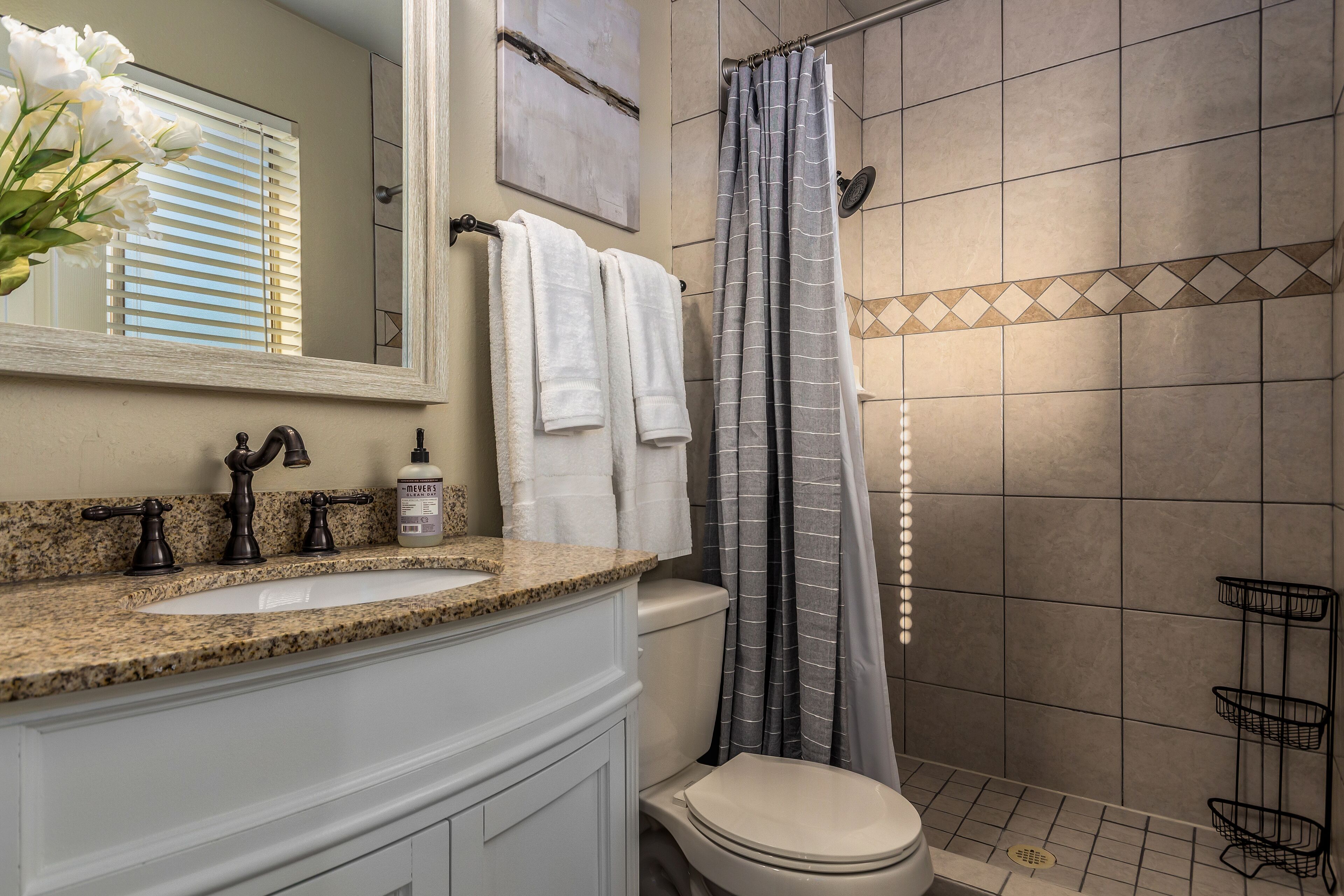 A bathroom with a granite countertop, a white sink, a toilet, and a shower with a striped curtain.