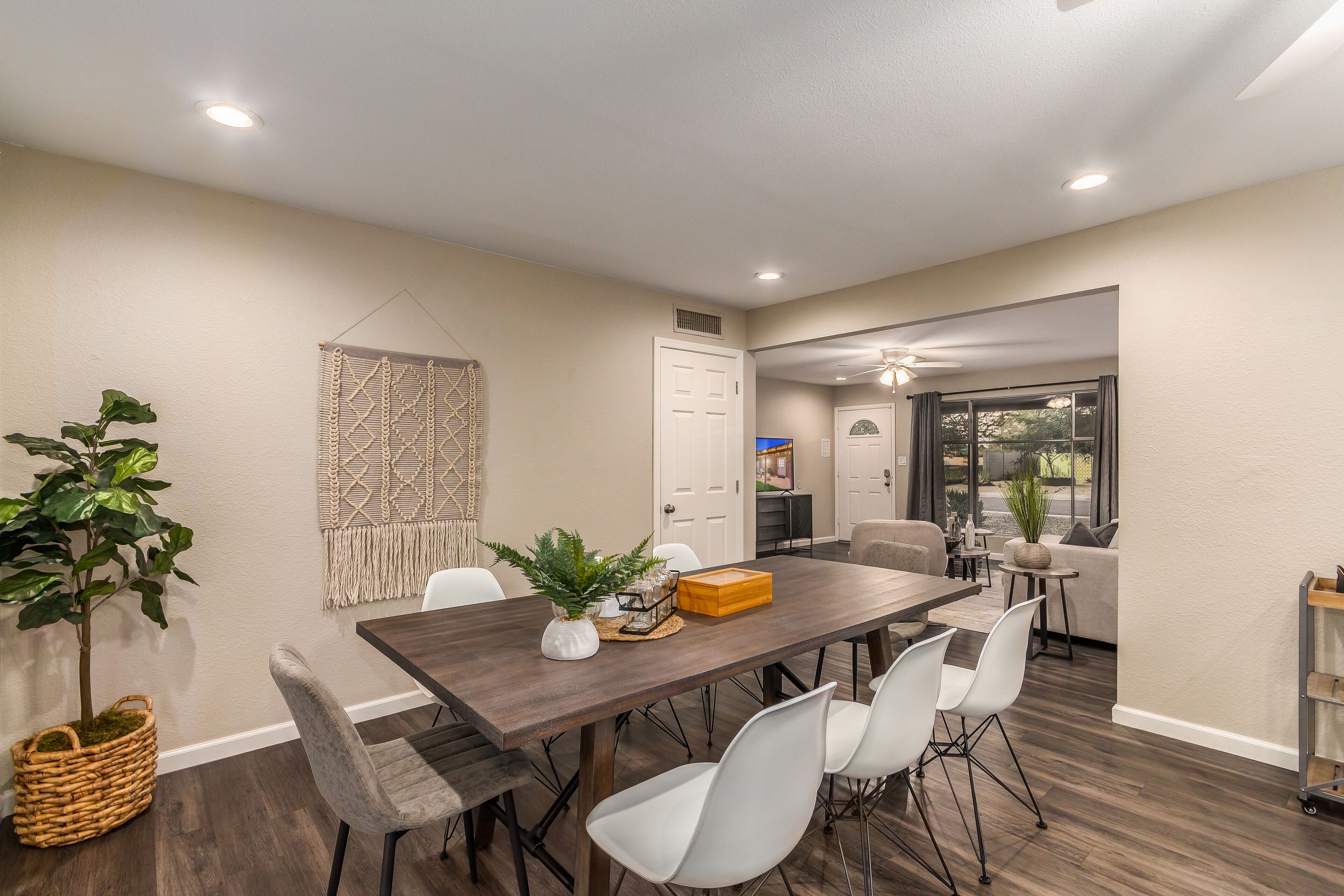 A dining area with a wooden table, white chairs, and a plant.
