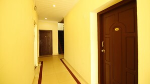 A hallway with a brown door marked with the number 101, a white ceiling, and a red stripe on the floor. - Lumino Highrange (Devikolam)