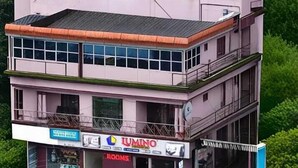 A multi-story building with a prominent 'LUMINO' sign, surrounded by lush green hills and a well-maintained garden. - Lumino Highrange (Devikolam)