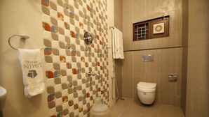 A bathroom with a checkered tile wall, a toilet, a shower, and a towel rack. - Lumino Highrange (Devikolam)