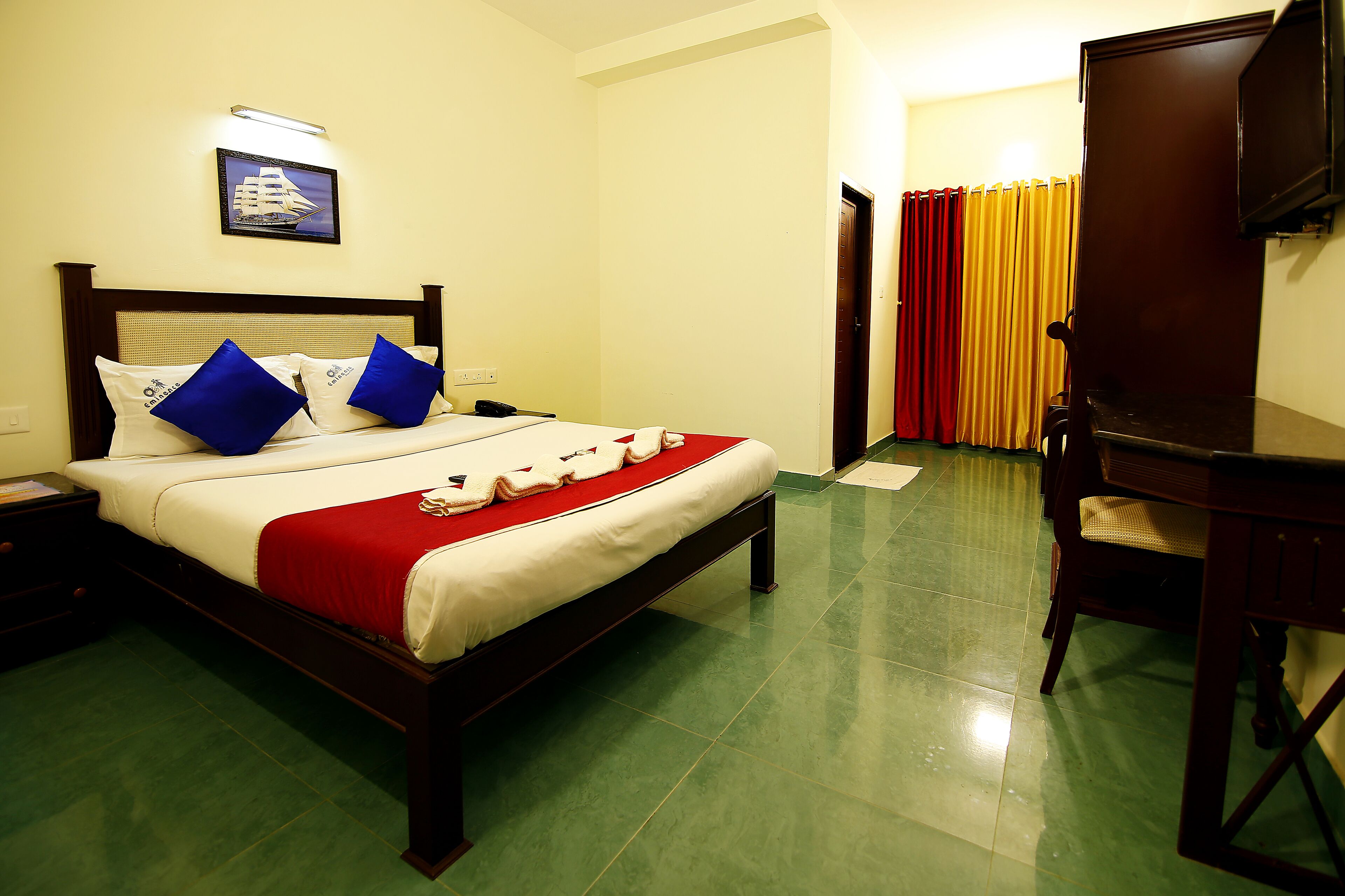 A hotel room with a bed, a desk, a chair, a television, and a curtain.
