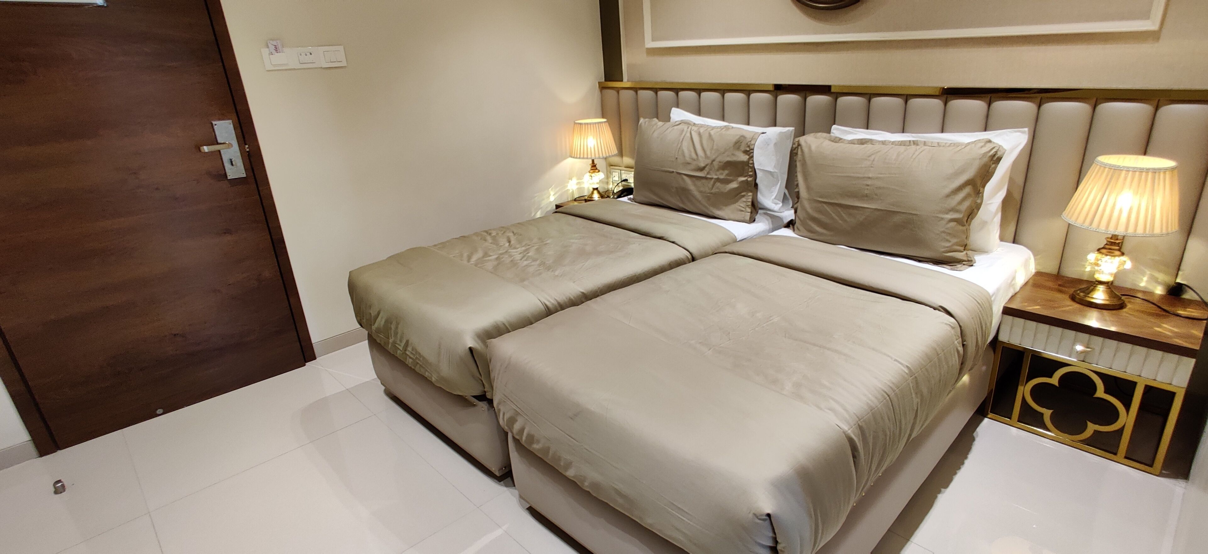 Una cama doble con ropa de cama color beige, una mesita de noche con una lámpara y una puerta de madera.