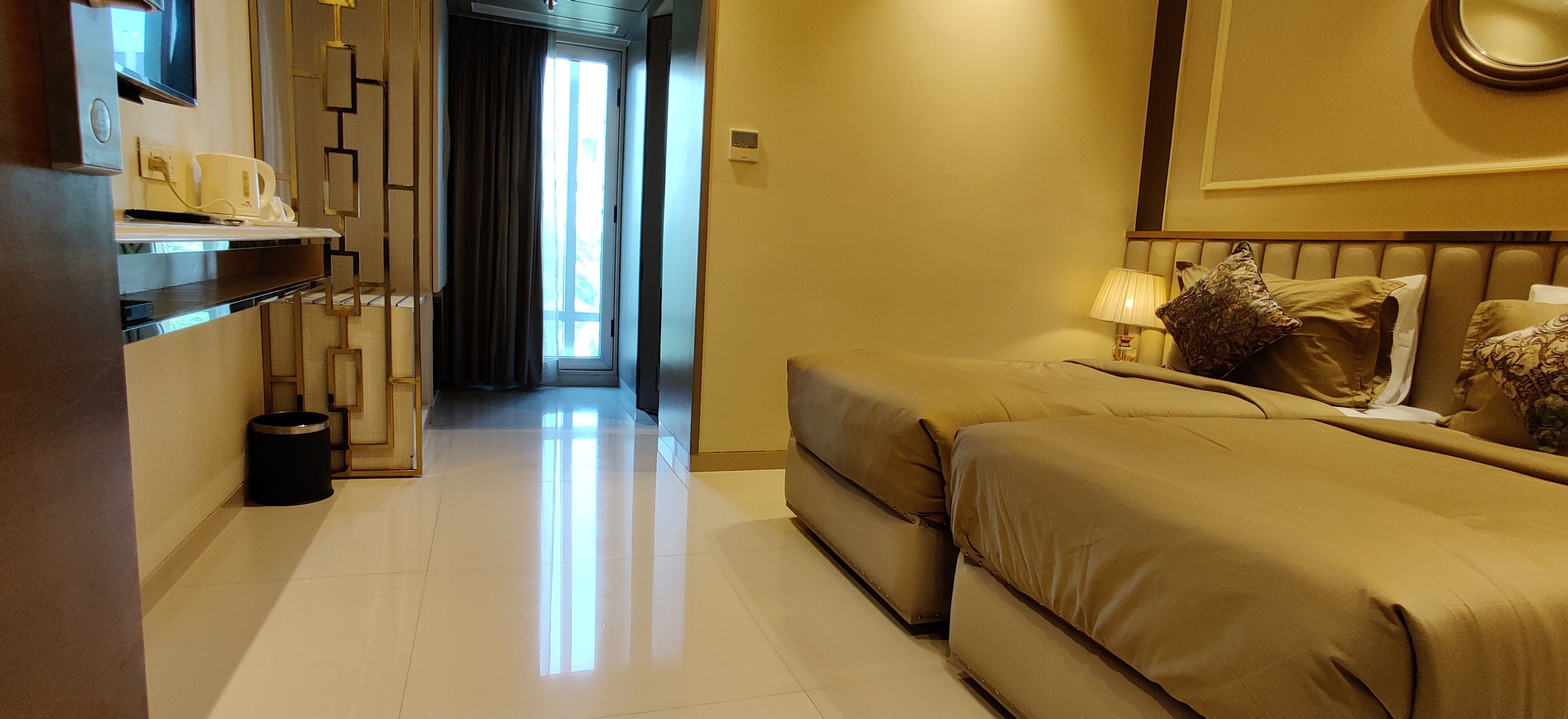 A hotel room with a bed, bedside table, lamp, and a view of a hallway.