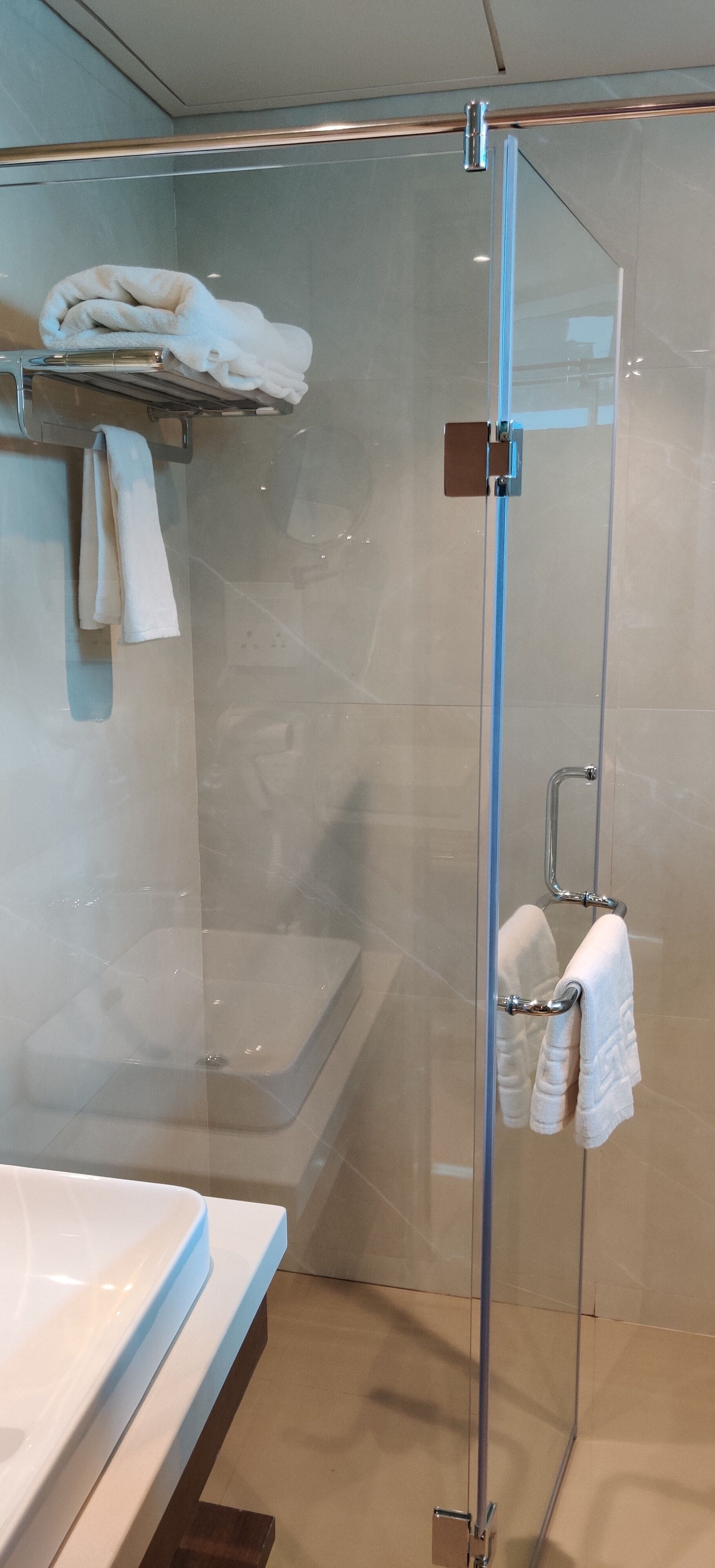 Un baño moderno con cabina de ducha de vidrio, un lavabo blanco y un perchero con toallas dobladas.