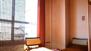 Habitación de esquina con ventana, una silla, una mesa y una mesita con tetera y taza.