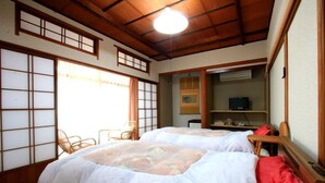 Una habitación tradicional japonesa con suelo de tatami, dos camas con ropa de cama floral, un televisor y una puerta corredera.