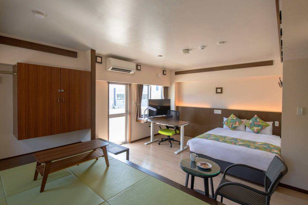 A hotel room with a bed, a desk with a chair, a television, a wardrobe, and a small table with a chair.