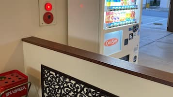 A vending machine with a variety of beverages and snacks, a red emergency button, and a metal chair with a decorative backrest.
