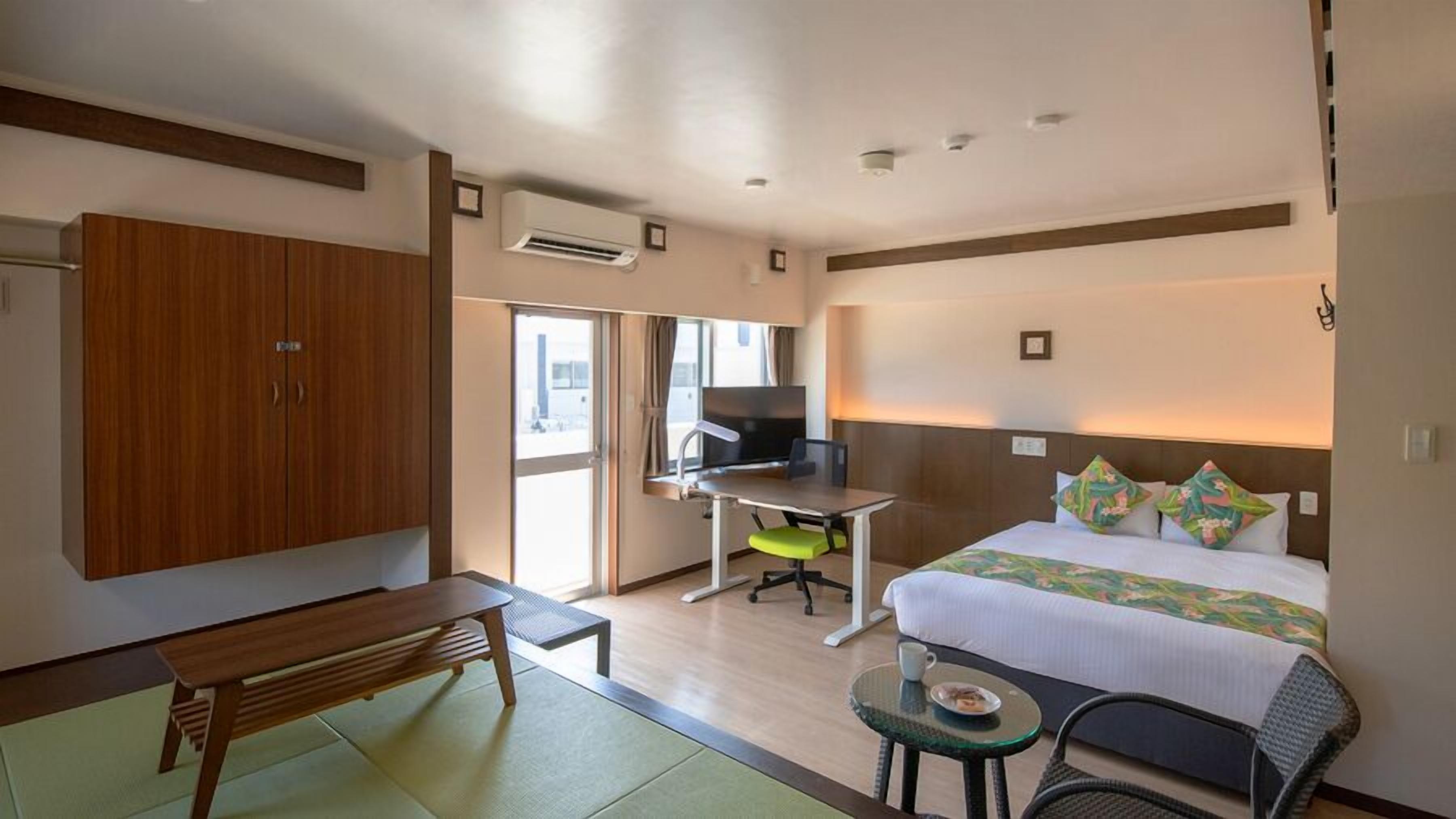 Une chambre d’hôtel comprenant un lit, un bureau, une chaise, une armoire et une petite table avec une tasse.