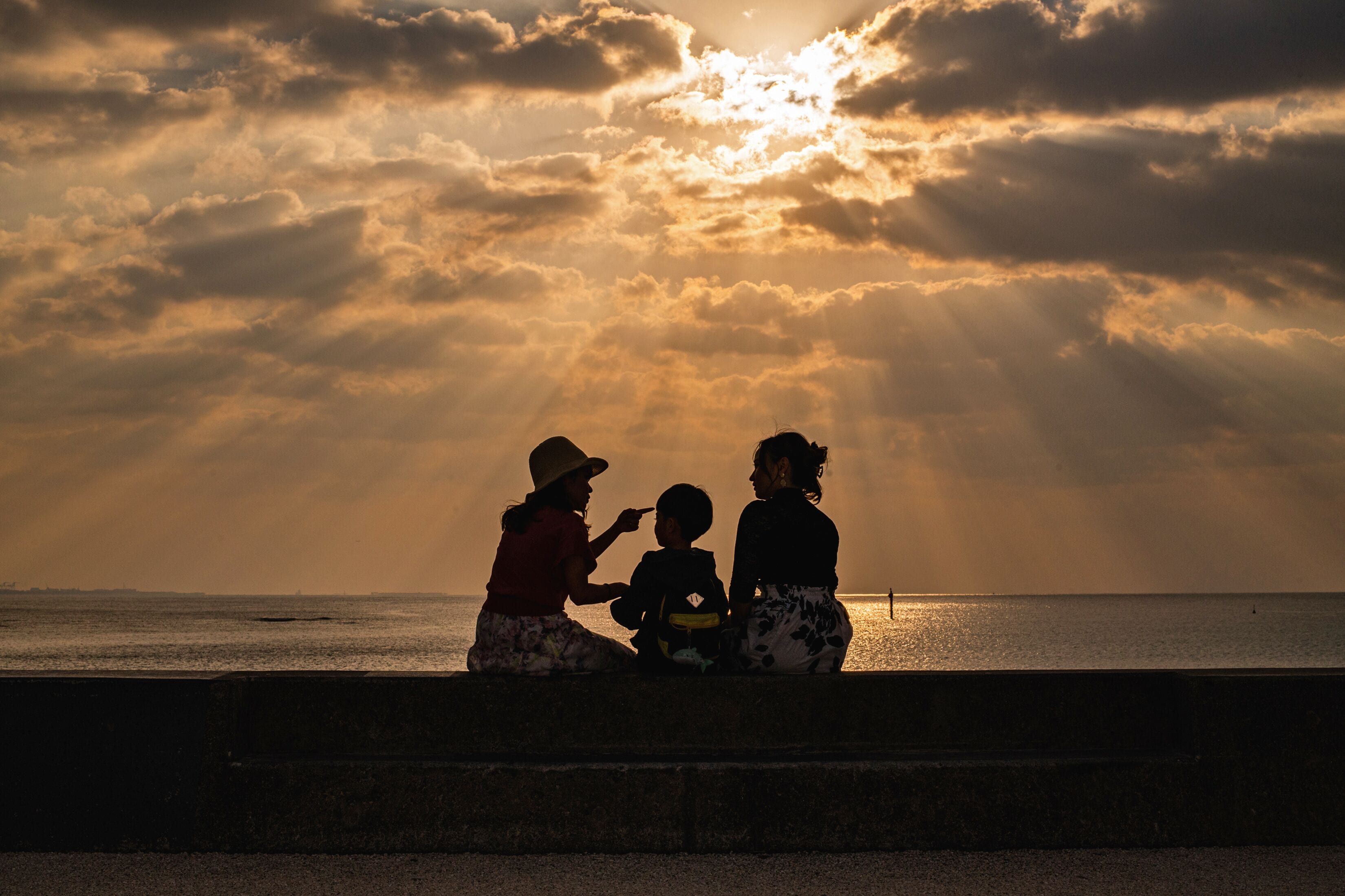 A sunset over a body of water with silhouettes of three people sitting on a ledge.
