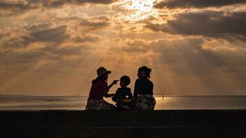 A sunset over a body of water with silhouettes of three people sitting on a ledge.