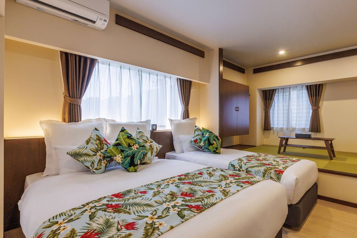 A hotel room with two beds, a desk, and an air conditioning unit.