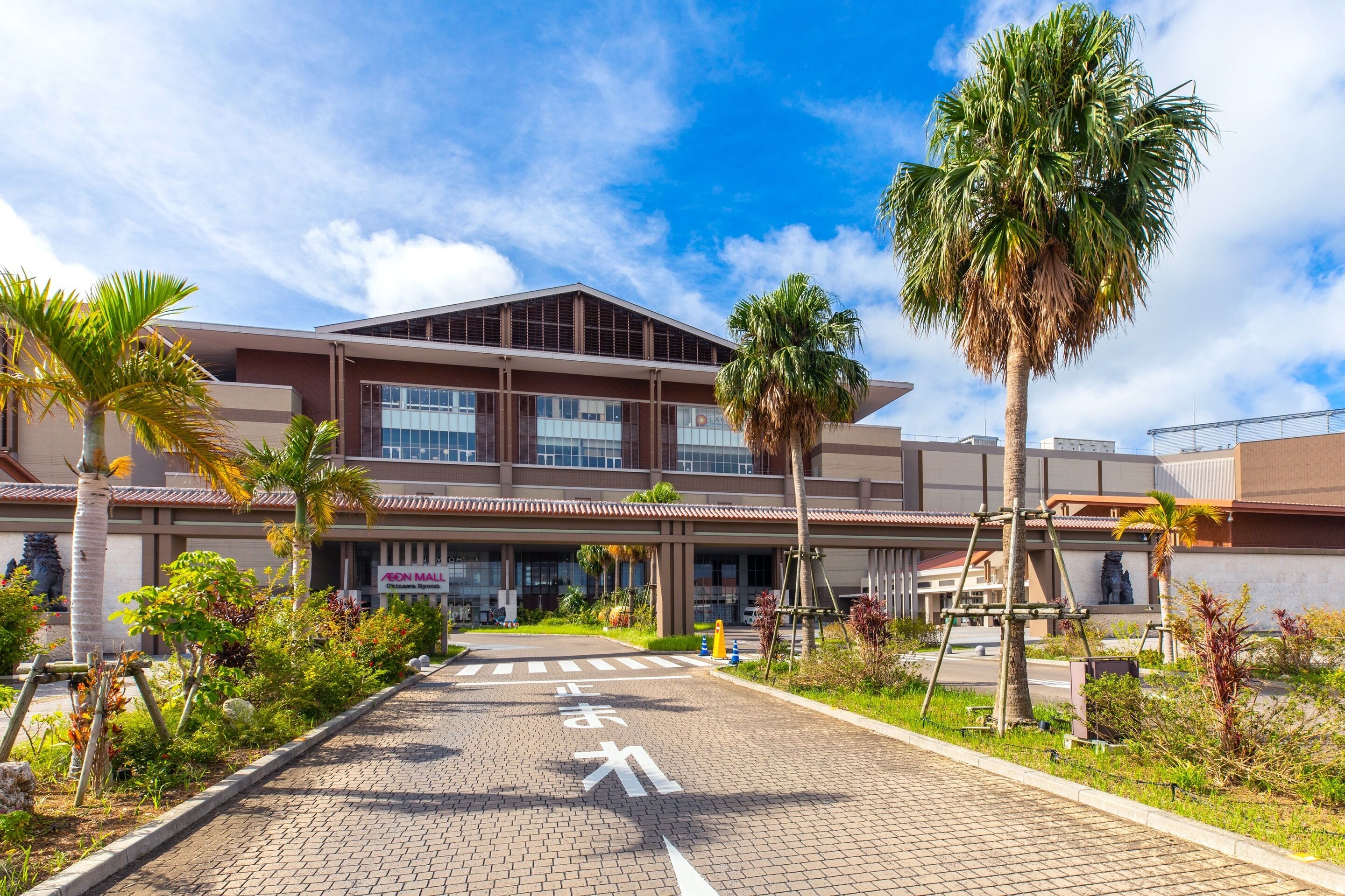 A modern building with a tiled entrance, palm trees, and a clear sky.