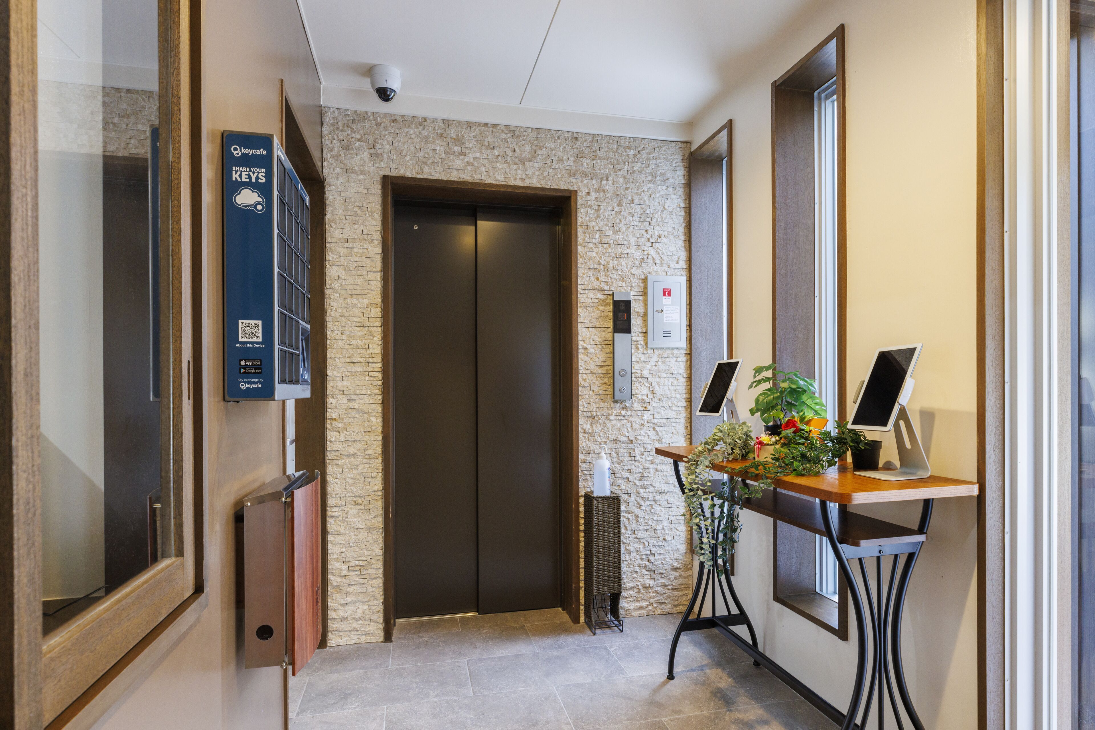 A hotel lobby with a reception desk, a digital screen, a security camera, and a door with a keypad lock.