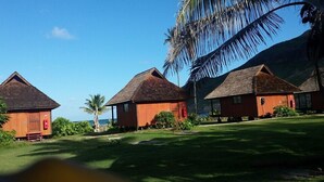 A row of wooden cabins with pitched roofs, surrounded by lush greenery and a clear blue sky. - Hakamoui Plage (Ua Pou)