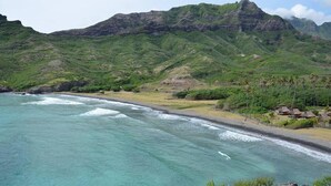 A coastal landscape with a beach, a mountain range, and a few houses. - Hakamoui Plage (Ua Pou)