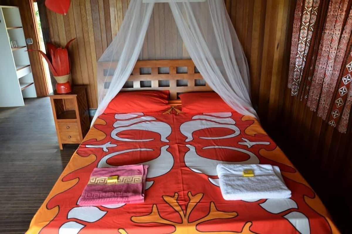 A bed with a canopy, a bedside table, a nightstand, and a red patterned bedspread.