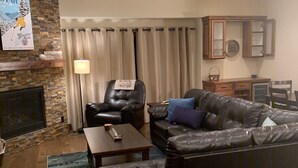 Ein Wohnzimmer mit Kamin aus Stein, einem Ledersessel, einer Ledersofa und einem Essbereich mit einem Holzschrank.