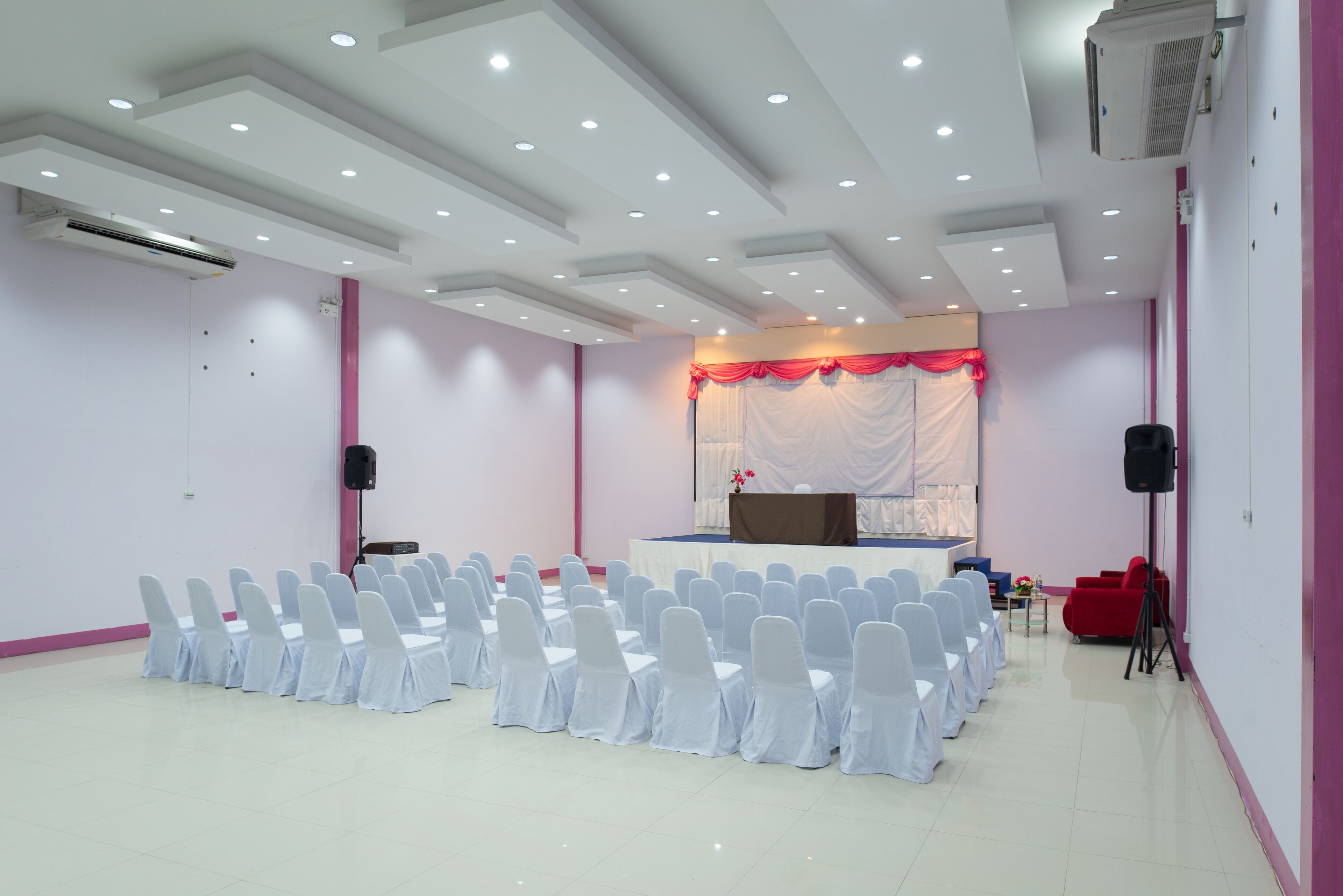 A conference room with rows of white chairs, a stage with a red curtain, and a podium.