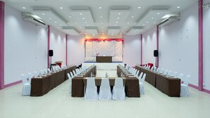 A conference room with a long table, white chairs, and a stage at the front. - Eco Inn Lite Chanthaburi (Chanthaburi)
