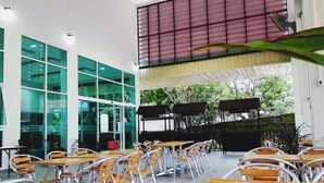A spacious indoor area with multiple tables and chairs, large windows, and a view of greenery outside. - Eco Inn Lite Chanthaburi (Chanthaburi)