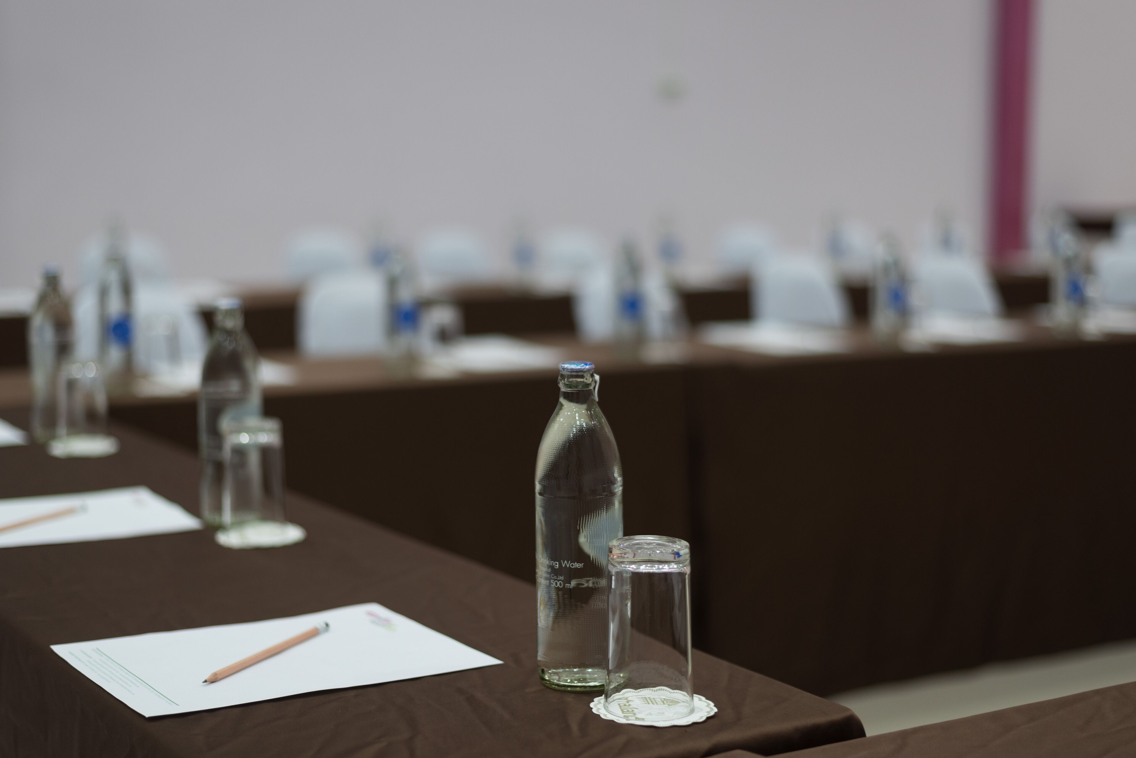 A conference room with tables set up for a meeting. Each table has a bottle of water, a glass, and a notepad with a pencil.