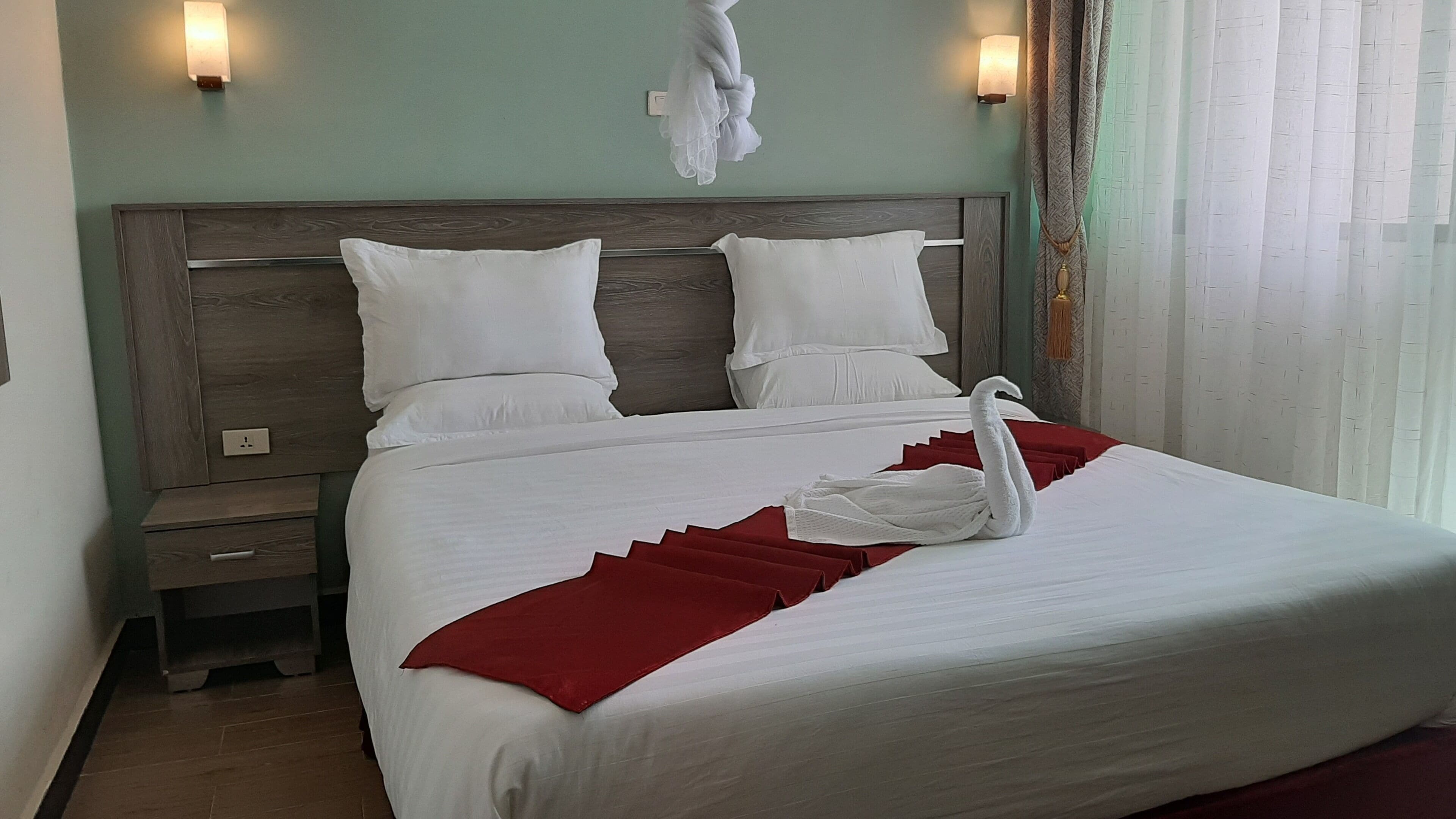 A neatly made bed with white linens and a red blanket, a wooden headboard, and two wall-mounted light fixtures.