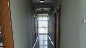 A long, narrow hallway with a tiled floor, a wooden door on the left, and a window at the end.