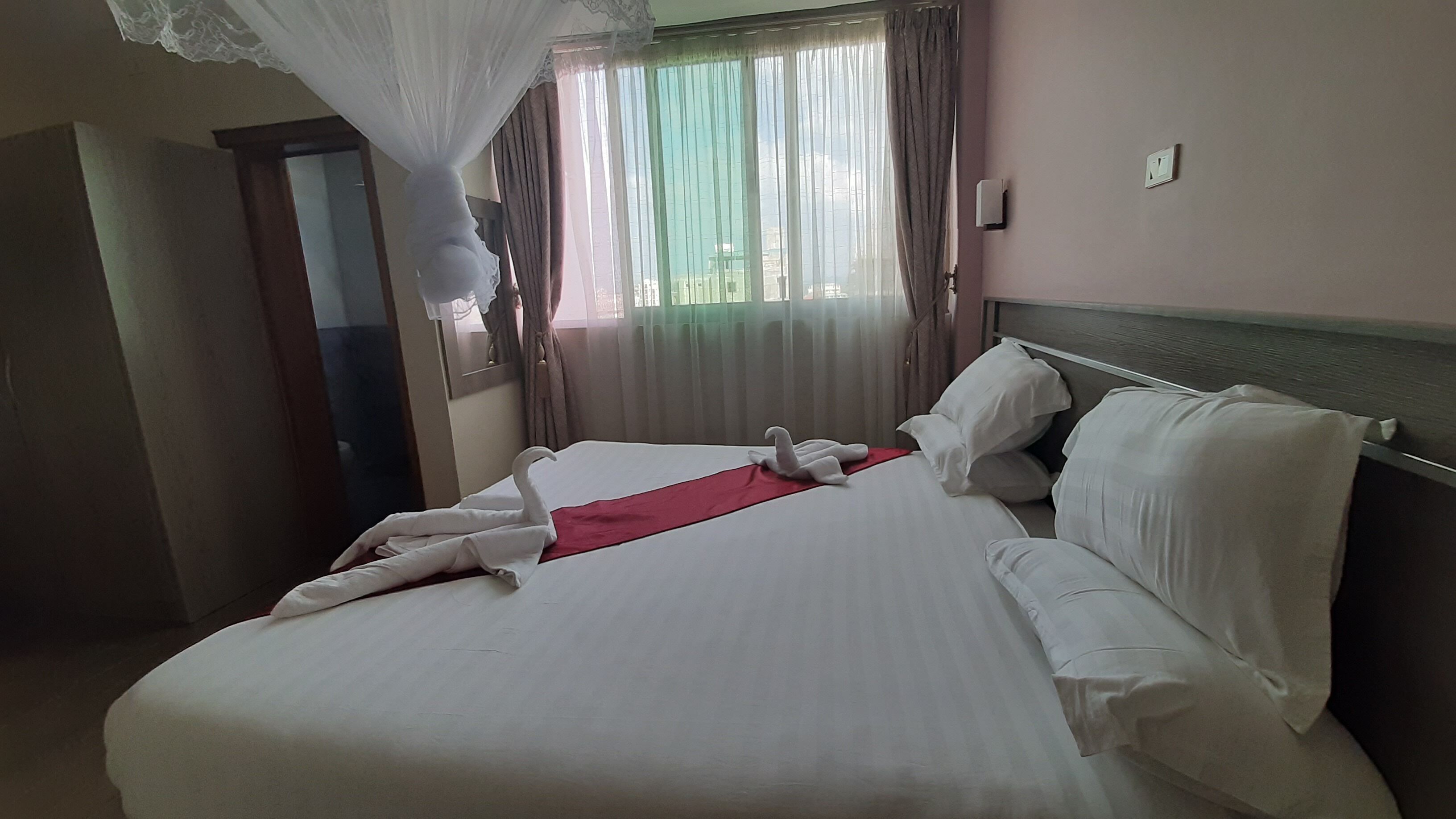 A hotel room with a large bed, white linens, a red accent pillow, and a canopy bedspread.