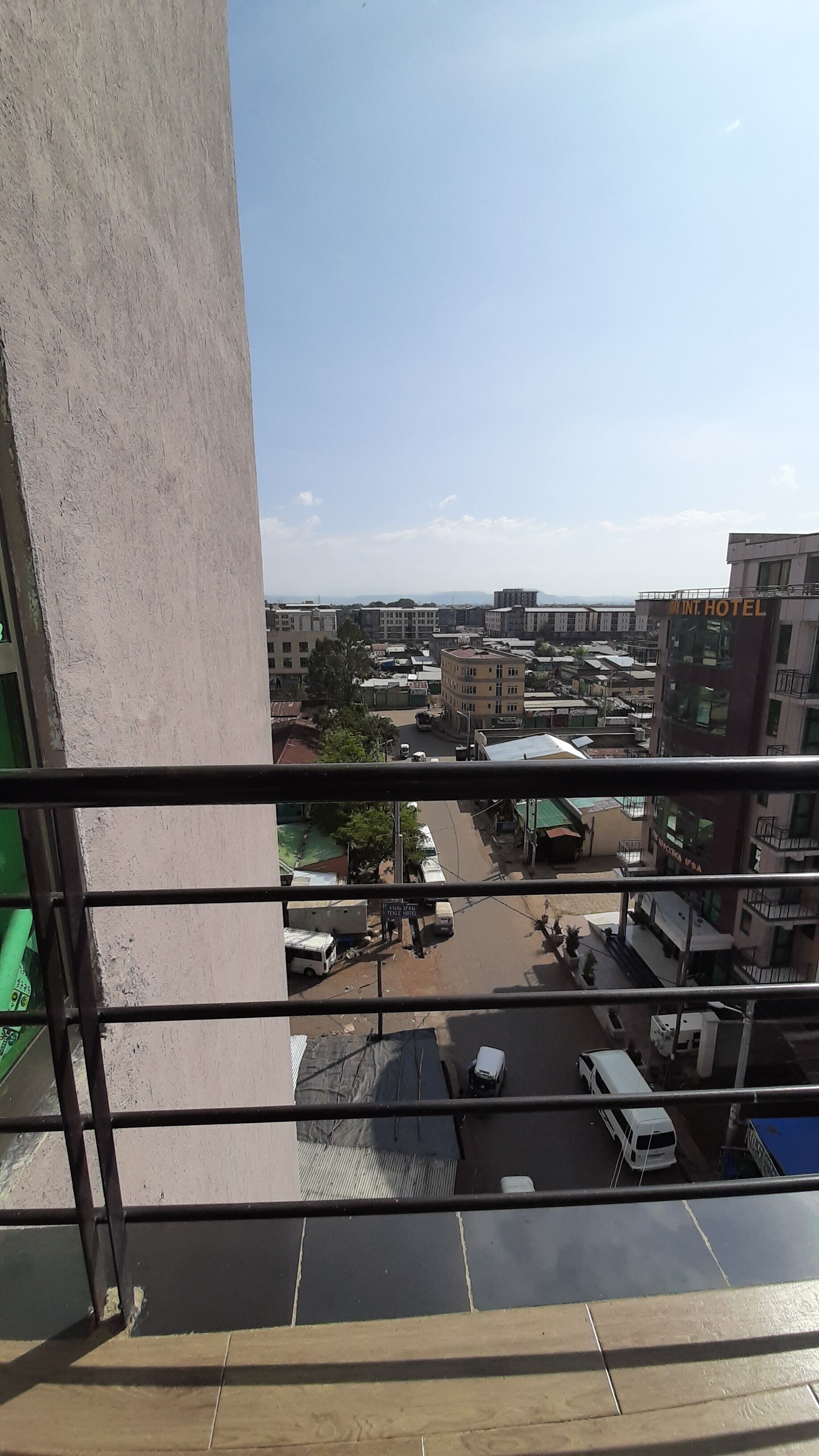 Vista desde un balcón sobre un paisaje urbano con edificios, una carretera y un aparcamiento.