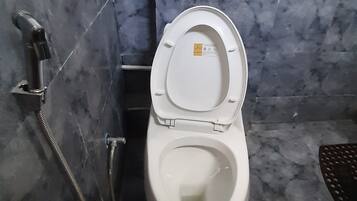 Un baño con inodoro, secamanos y desagüe en el suelo.