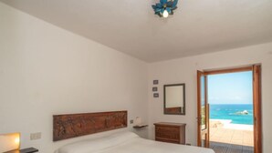 A bedroom with a bed, a dresser, a mirror, and a view of the ocean through an open door. - Sa Murta by Interhome (Portobello)