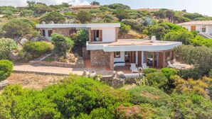 A modern villa with a stone facade, a covered patio with lounge chairs, and a lush, green hillside backdrop. - Sa Murta by Interhome (Portobello)