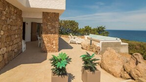 A modern building with stone walls and a patio area with lounge chairs and potted plants. - Sa Murta by Interhome (Portobello)