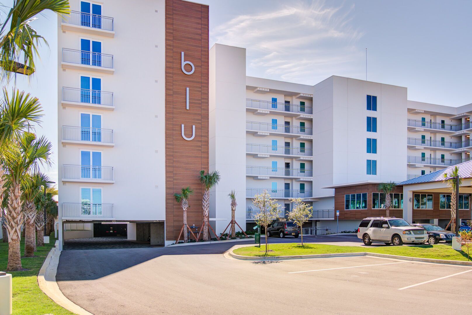 Een modern hotel met een opvallend 'bilu'-bord, meerdere balkons en een parkeerplaats.