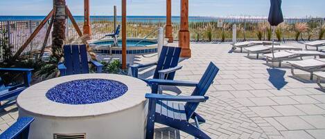 A beachside patio with a wooden pergola, lounge chairs, a hot tub, and a view of the ocean.