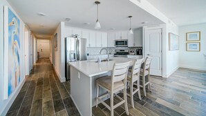 A modern kitchen with white cabinetry, a central island with bar stools, a stainless steel refrigerator, and a microwave.