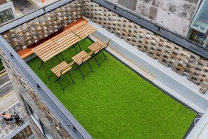 Un espace extérieur aménagé avec des bancs en bois et une pelouse artificielle verte.
