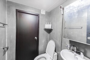 Une salle de bain avec une porte sombre, des toilettes blanches, un lavabo et un miroir. Il y a deux bouteilles sur une étagère au-dessus des toilettes.