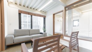 Un intérieur moderne avec un canapé gris, des chaises en bois et une grande fenêtre donnant sur l’extérieur.